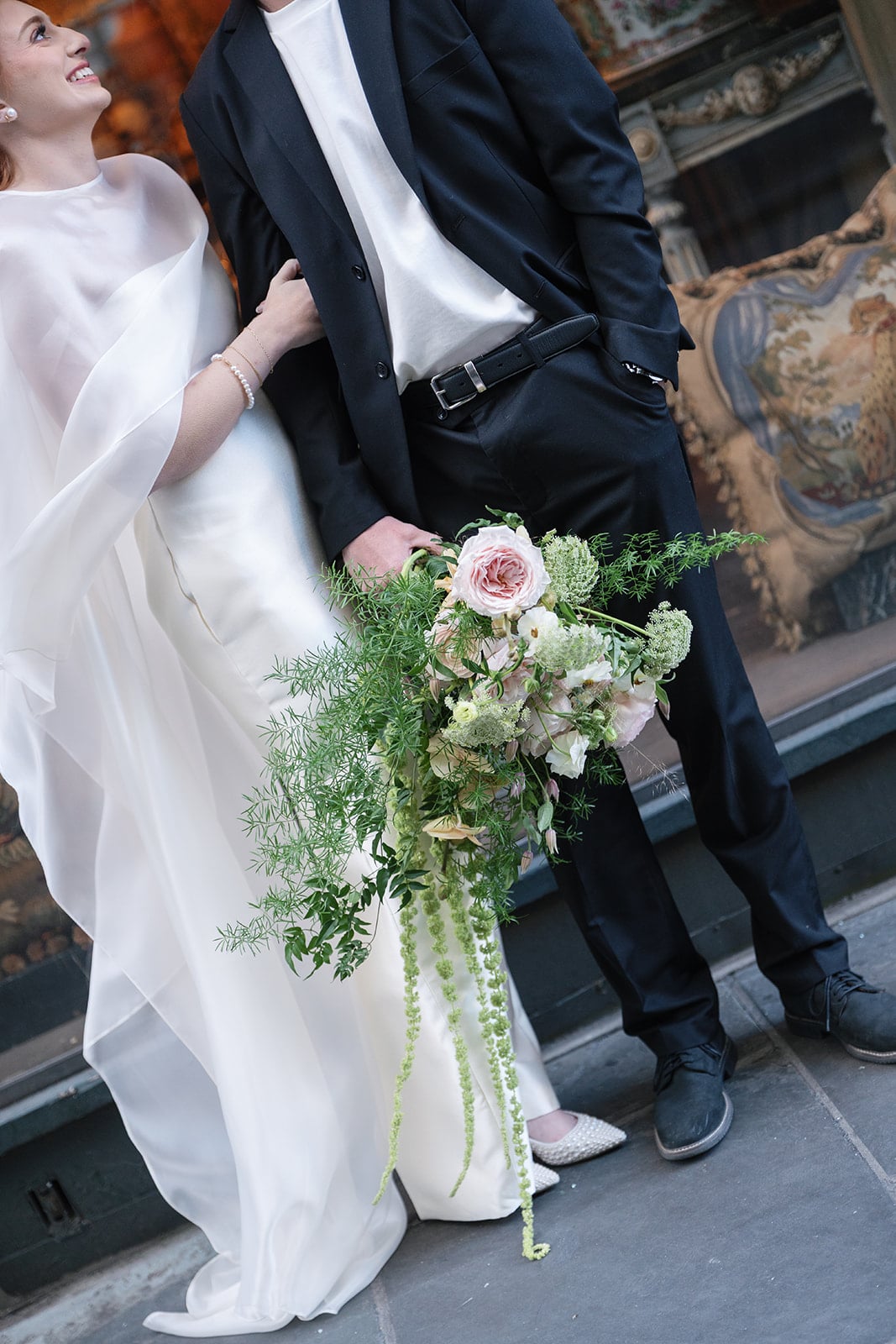 Elegant wedding couple holding a cascading floral bouquet with pink roses in a historic New Orleans setting.