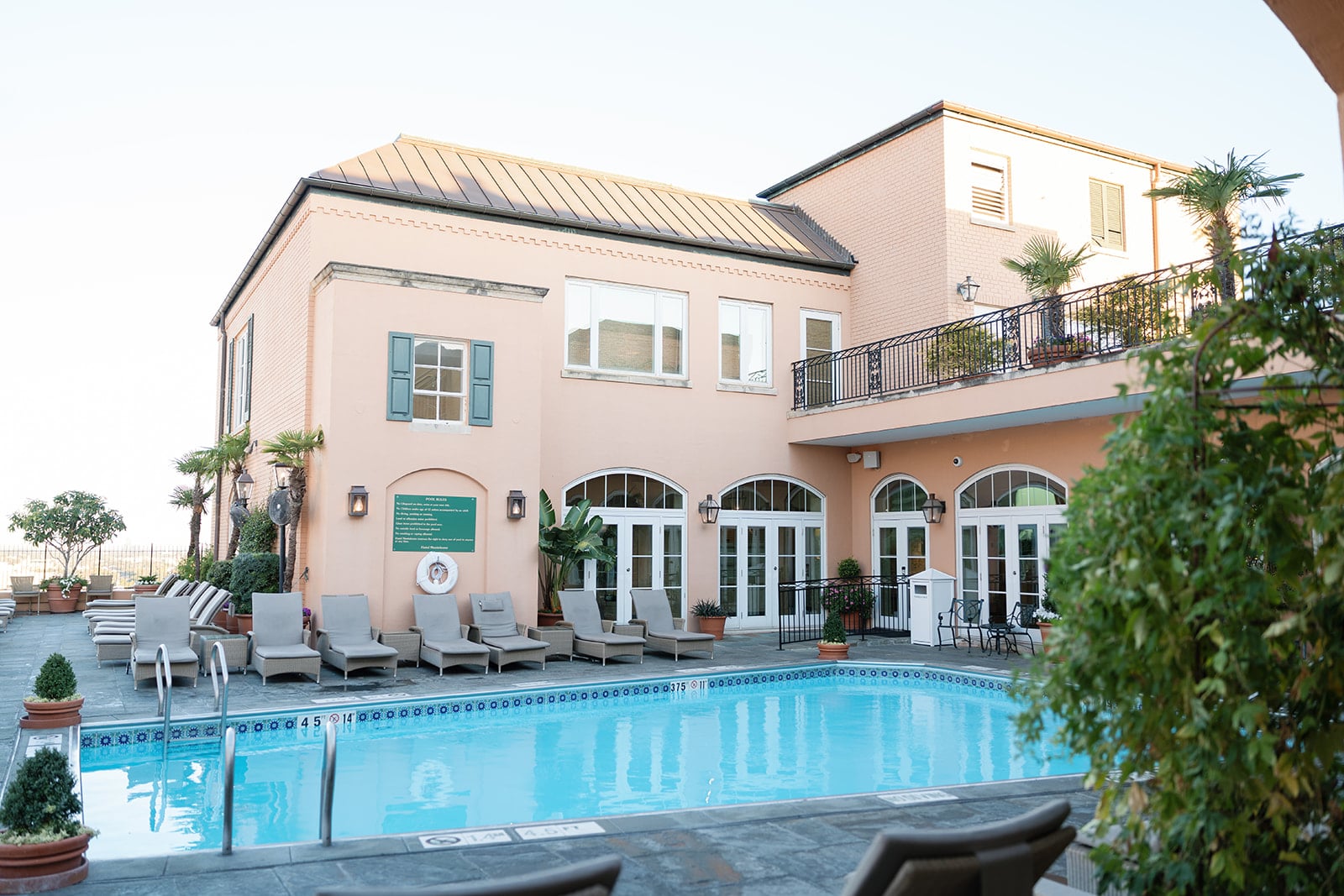 Charming New Orleans hotel pool area with a peach-colored building, balcony, and comfortable lounge chairs.