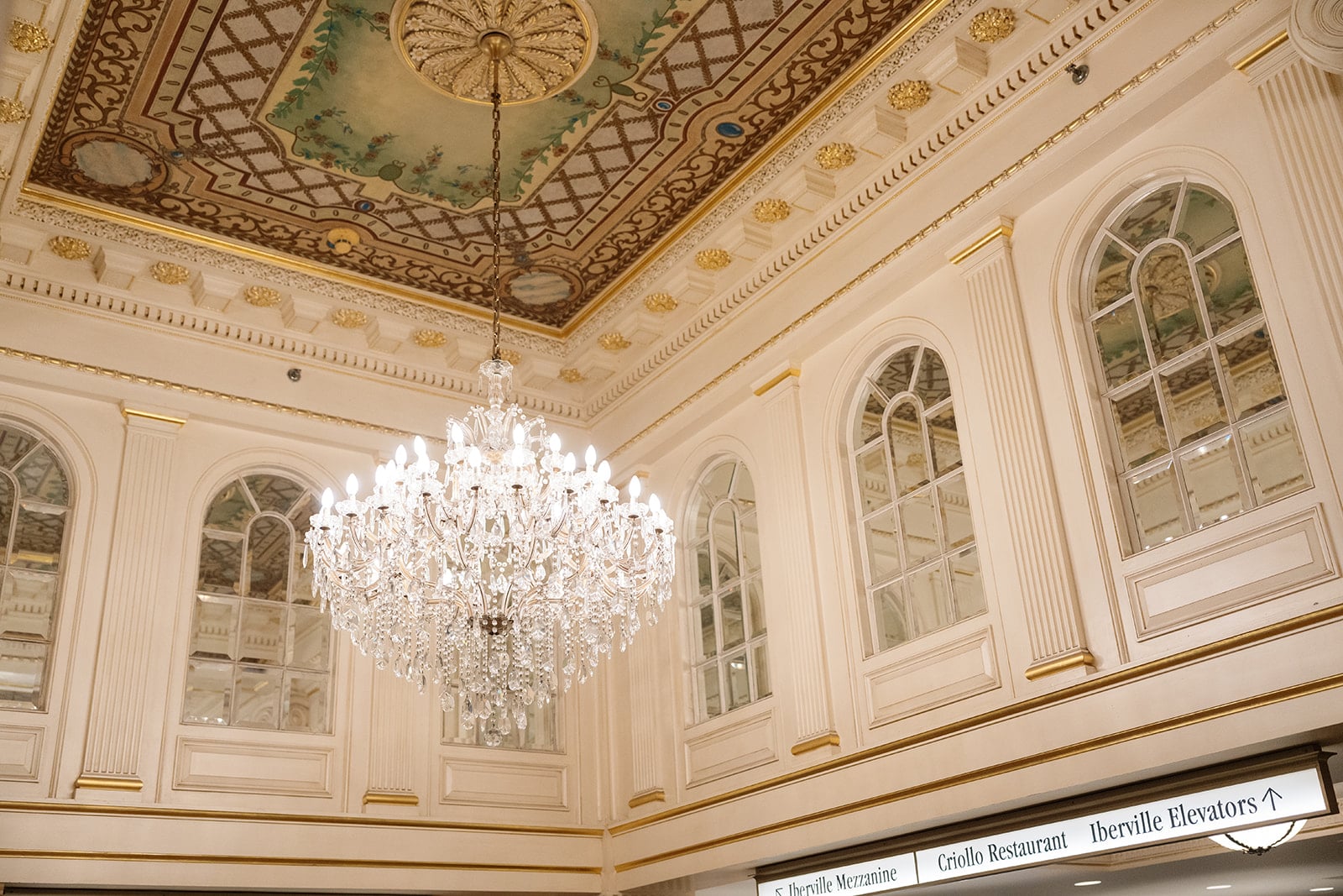 Elegant New Orleans hotel lobby with a grand crystal chandelier, ornate painted ceiling, and arched windows.