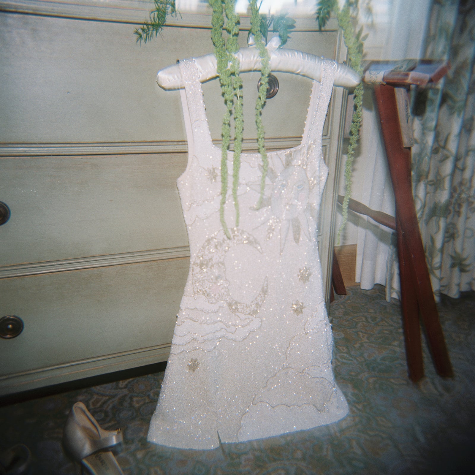 Sparkling white dress with sun, moon, and stars design, adorned with green garland, in a New Orleans room.