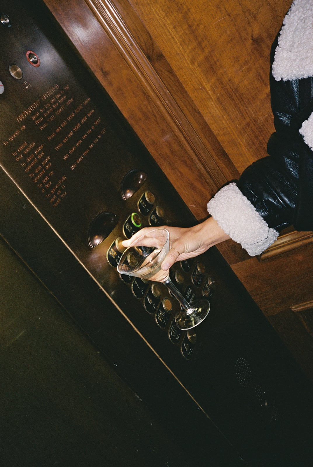 Person with a martini presses an elevator button in a luxurious New Orleans hotel.