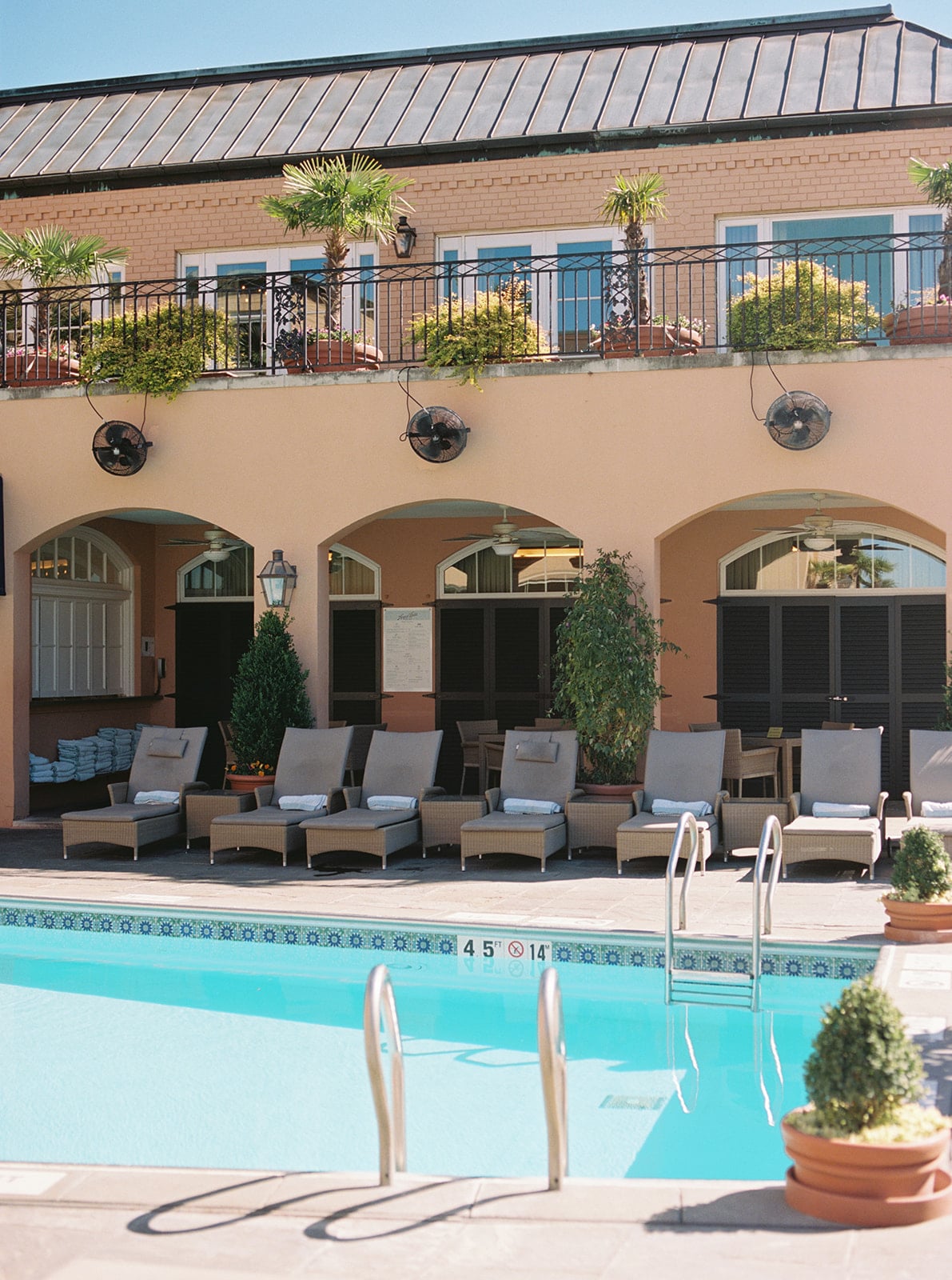 New Orleans hotel pool with lounge chairs, palm trees, and classic archways.