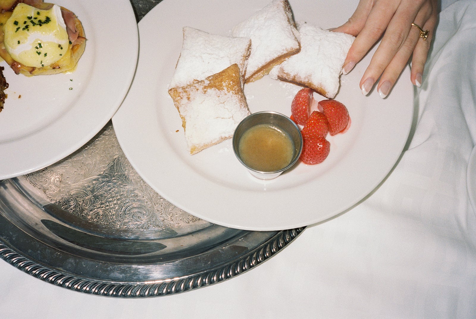 Classic New Orleans breakfast in bed: beignets with powdered sugar, fresh strawberries, syrup, and Eggs Benedict.