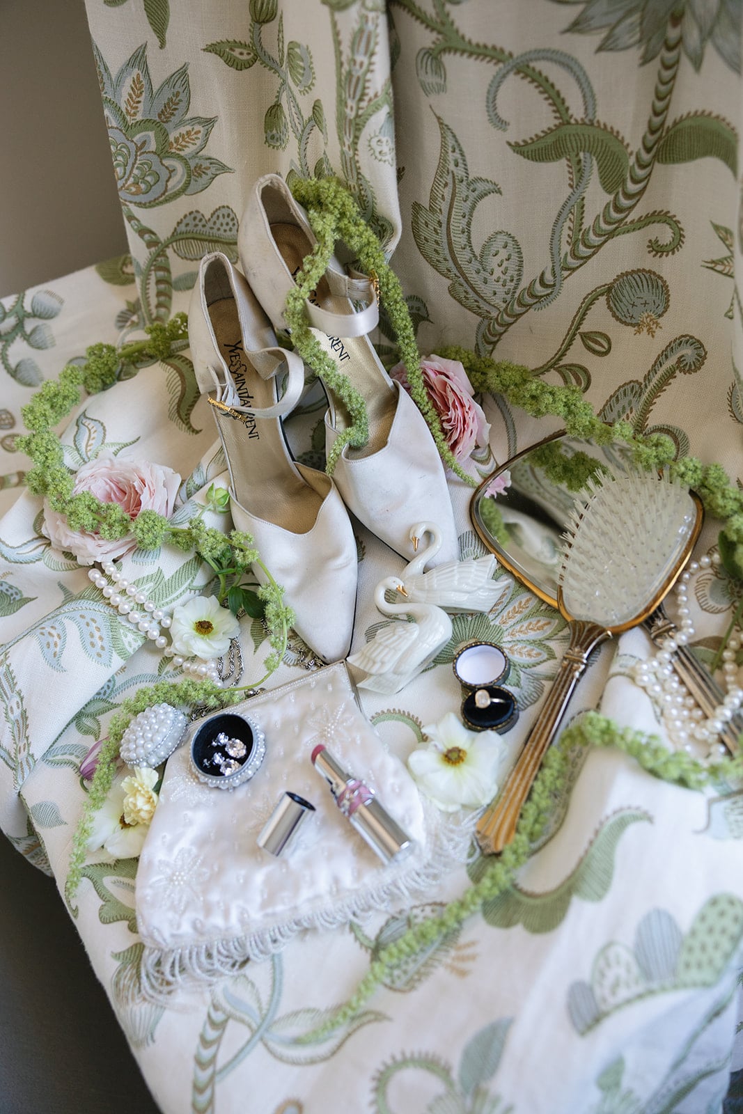 Vintage style bridal accessories, YSL heels, pearls, lipstick, and swans on patterned fabric.