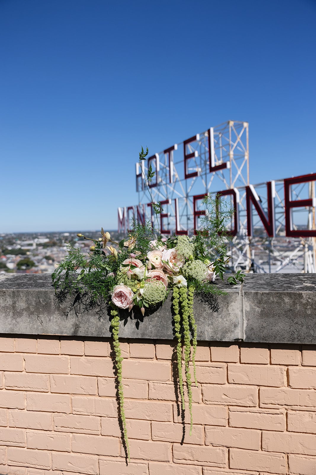 Rooftop bouquet with pink roses and trailing greenery, overlooking the Hotel Monteleone sign and New Orleans skyline.