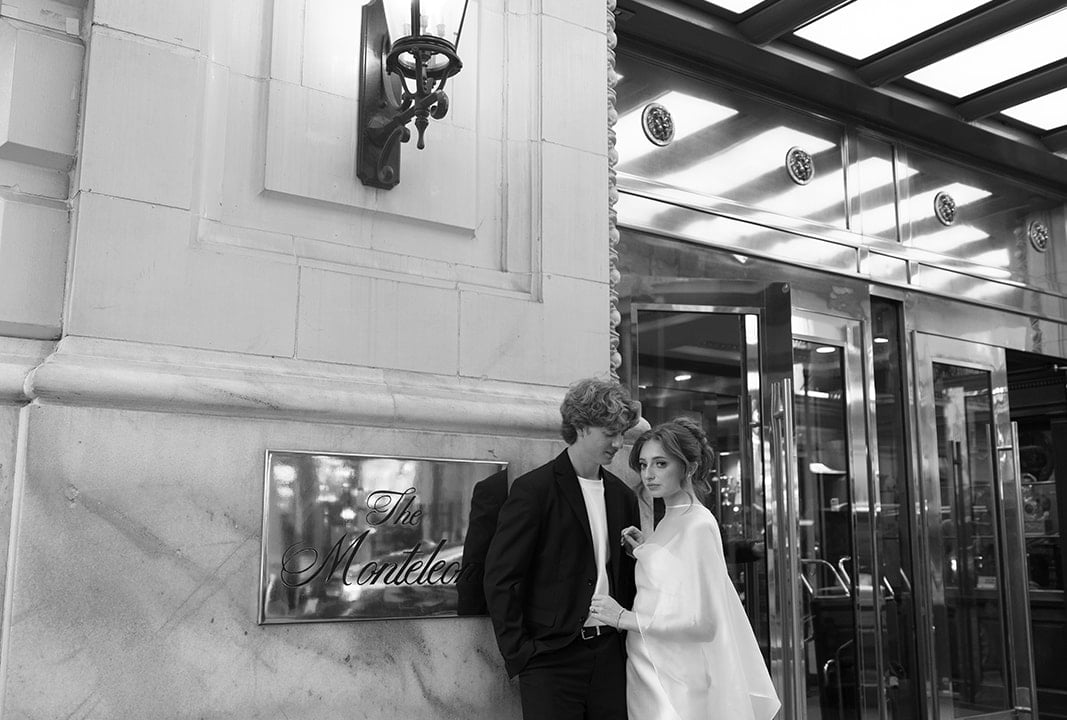 A black and white photo of a couple standing outside a building with a sign that reads 'The Monteleon'.