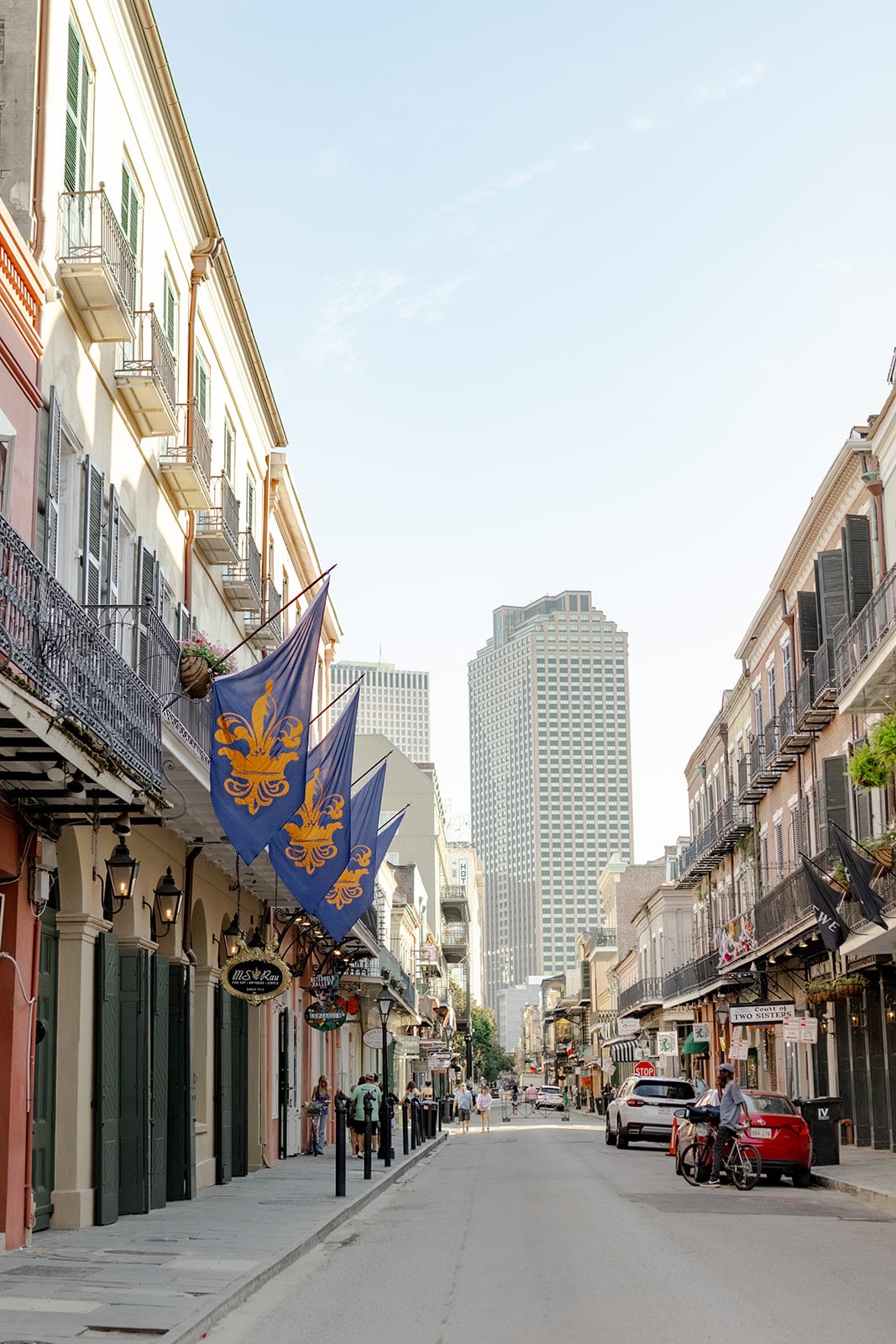 Bustling New Orleans French Quarter street with historic buildings, iron balconies, and fleur-de-lis flags.