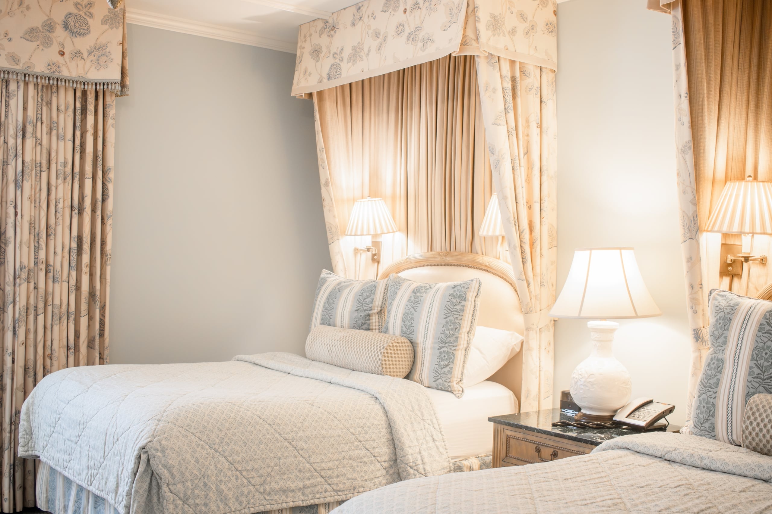 Elegant New Orleans hotel room featuring two beds, classic floral drapes, and warm lighting.