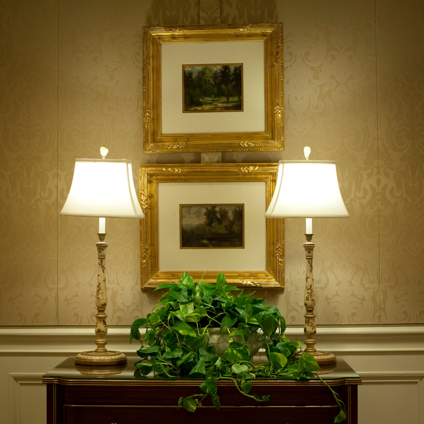 Classic hotel decor with elegant lamps, a lush plant, and gold-framed art.