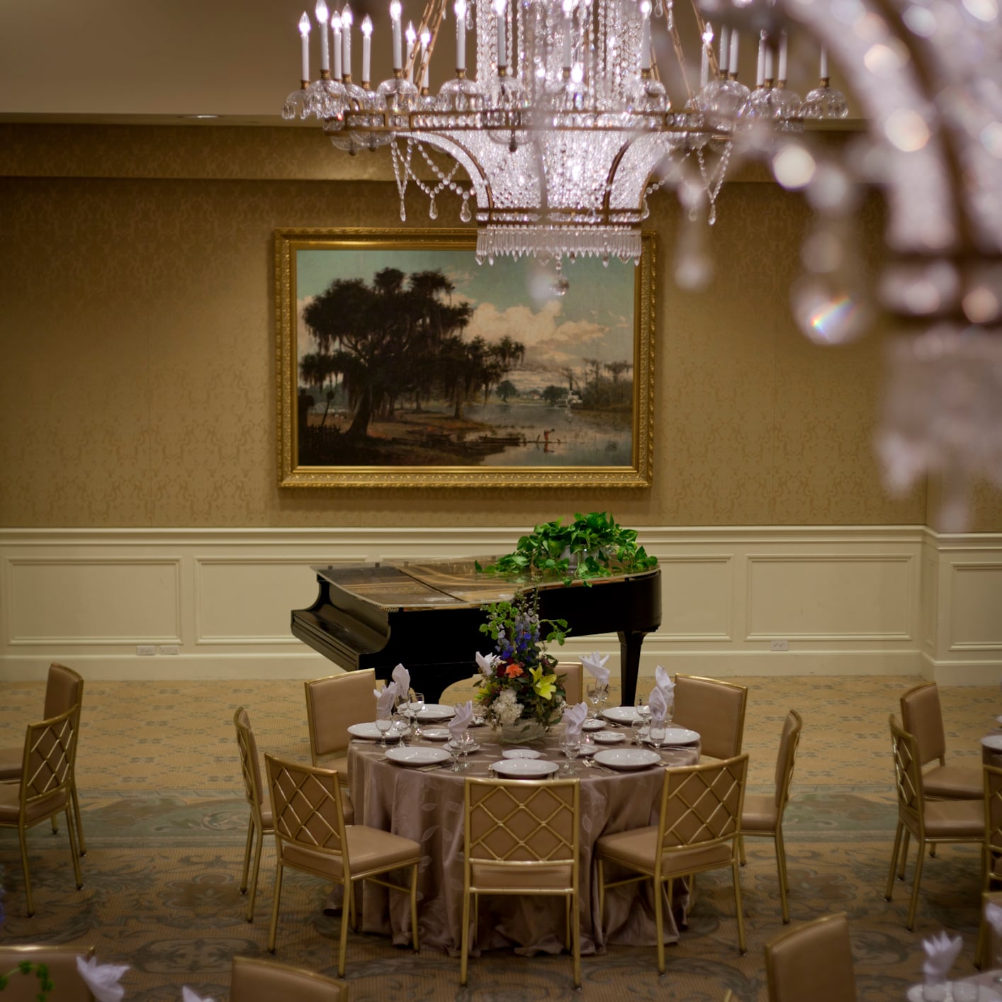 Elegant New Orleans ballroom with chandeliers, bayou painting, grand piano, and tables set for an event.