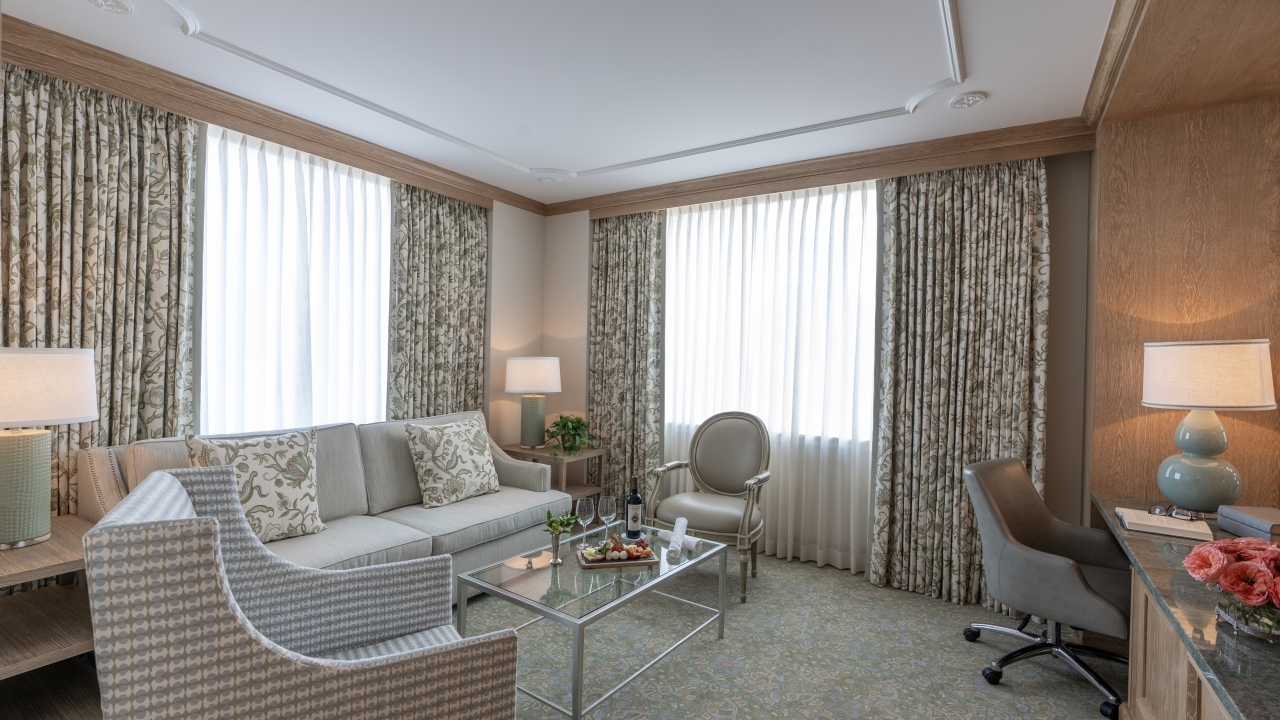 A wide view of a hotel suite's living area with a sofa, coffee table, desk, and chair.