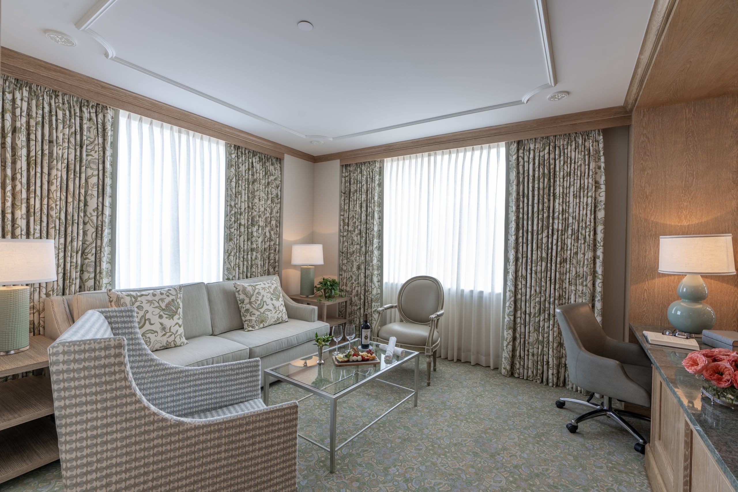 Elegant New Orleans hotel suite living area with comfortable seating, a workspace, and bright windows.