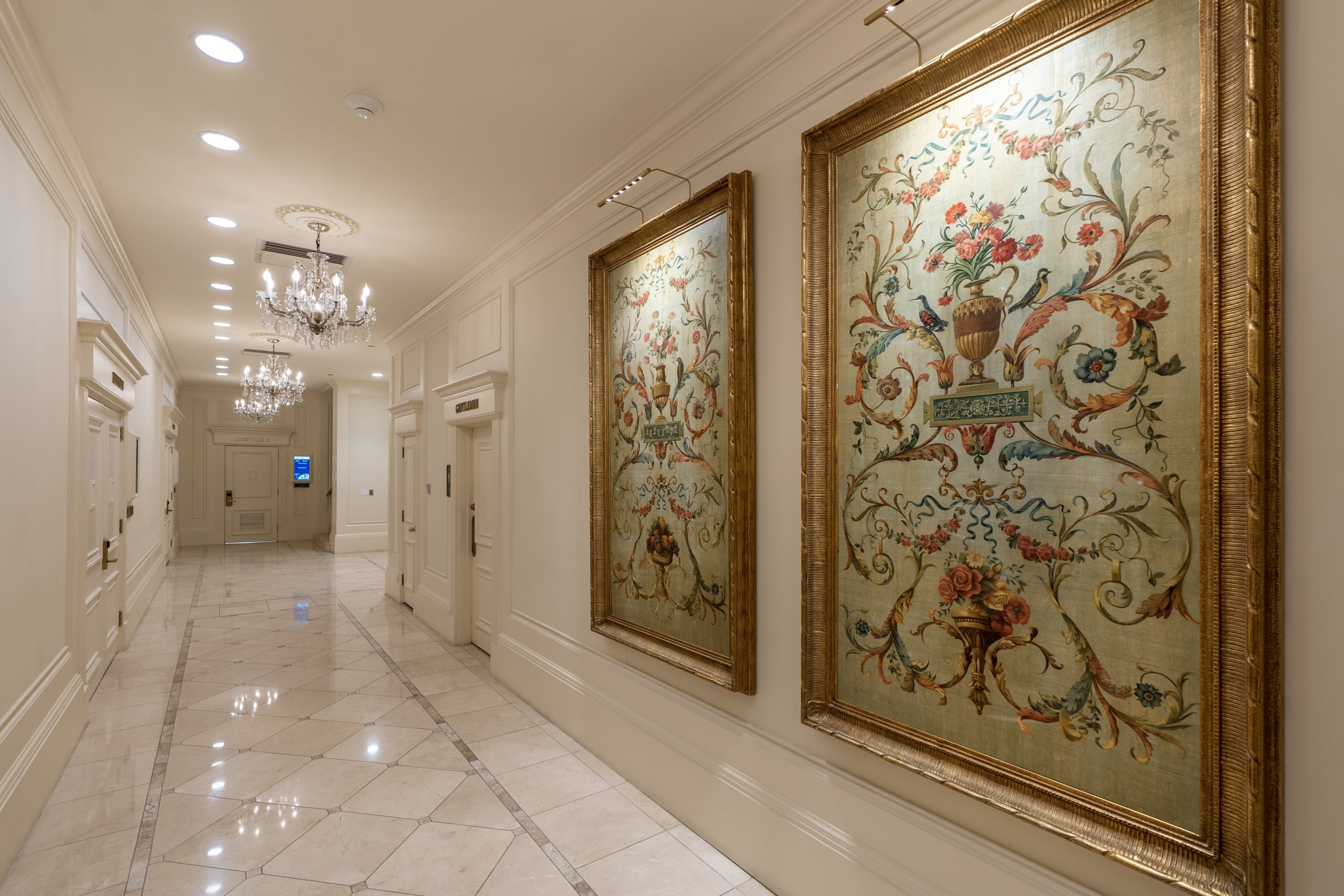 Grand New Orleans hotel hallway with ornate chandeliers, patterned marble floor, and framed classical art