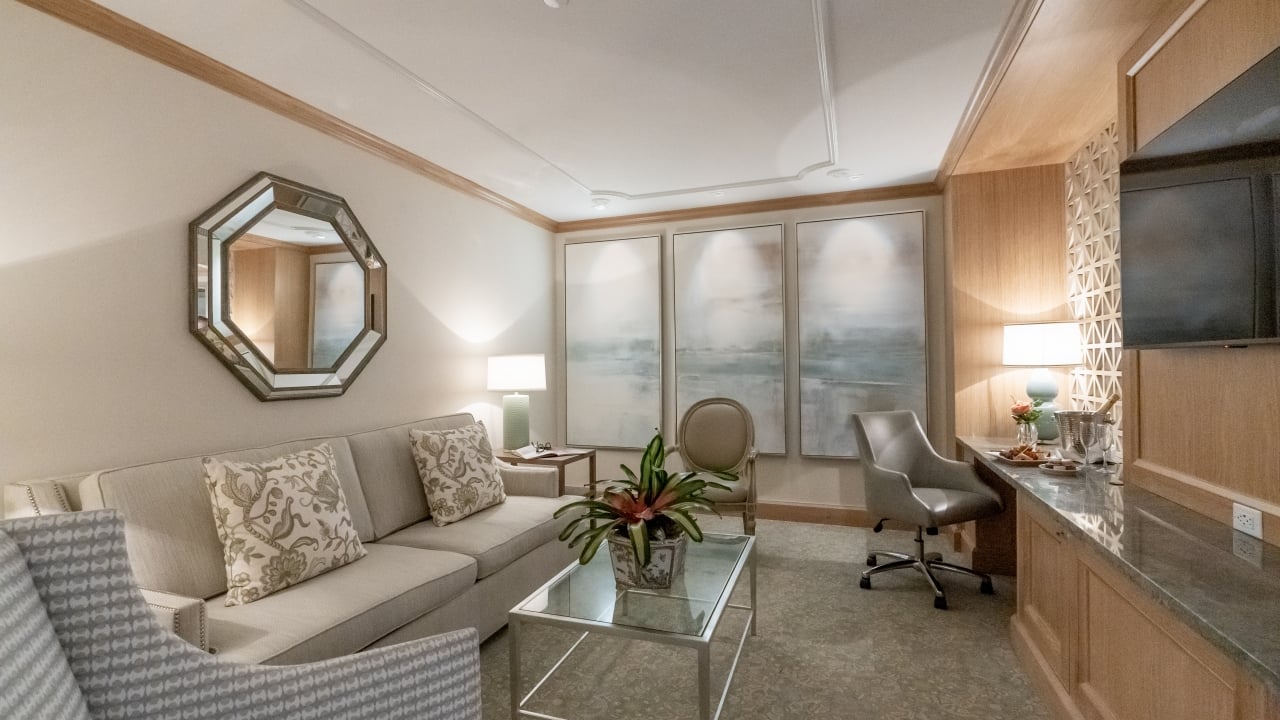 A wide view of a hotel suite with a sofa bed, desk, TV, and coffee table.