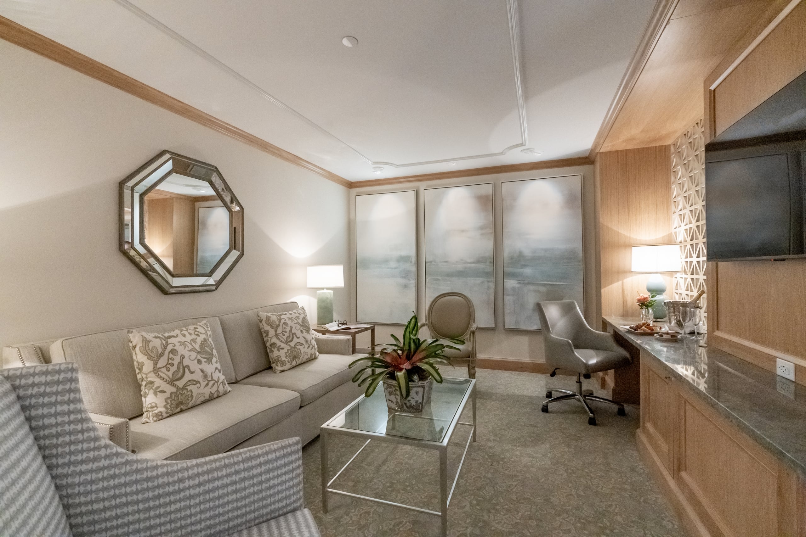 Modern living room in a New Orleans hotel suite with a beige sofa, mirrored wall decor, and a light wood wet bar.