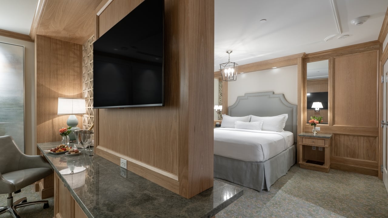 A hotel room with a king-sized bed, desk, and TV