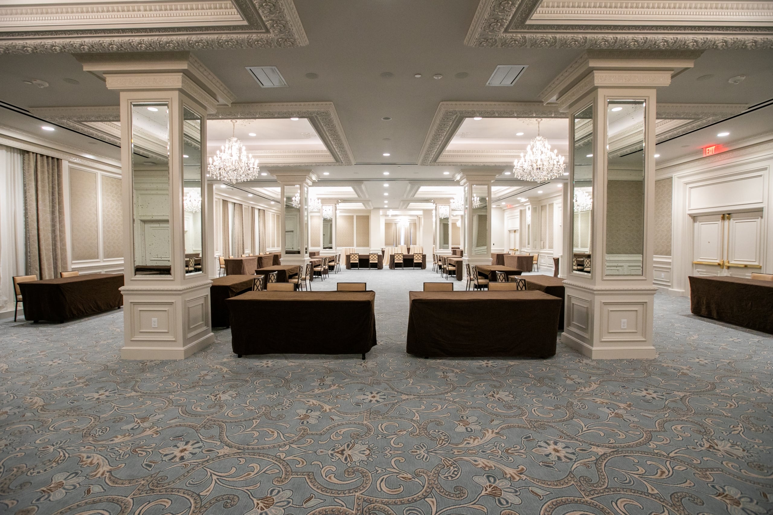 Luxurious New Orleans event space with ornate chandeliers, mirrored pillars, and brown covered tables.