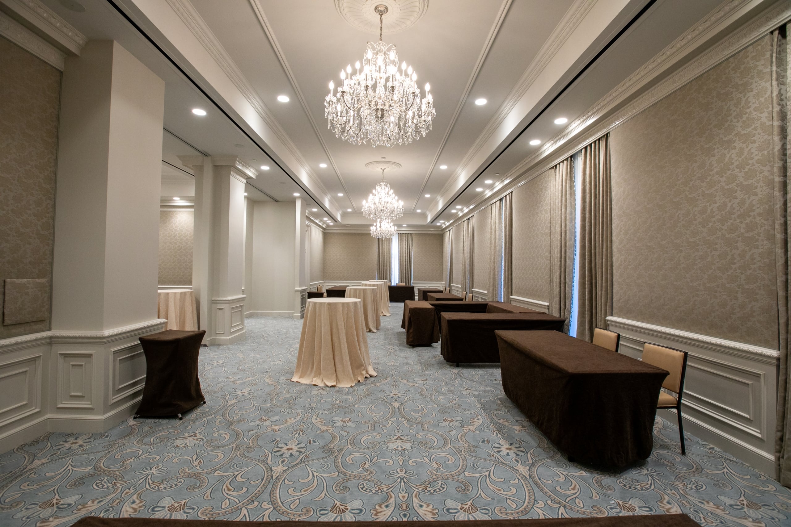 Elegant New Orleans reception hall with crystal chandeliers, blue patterned carpet, and draped tables.