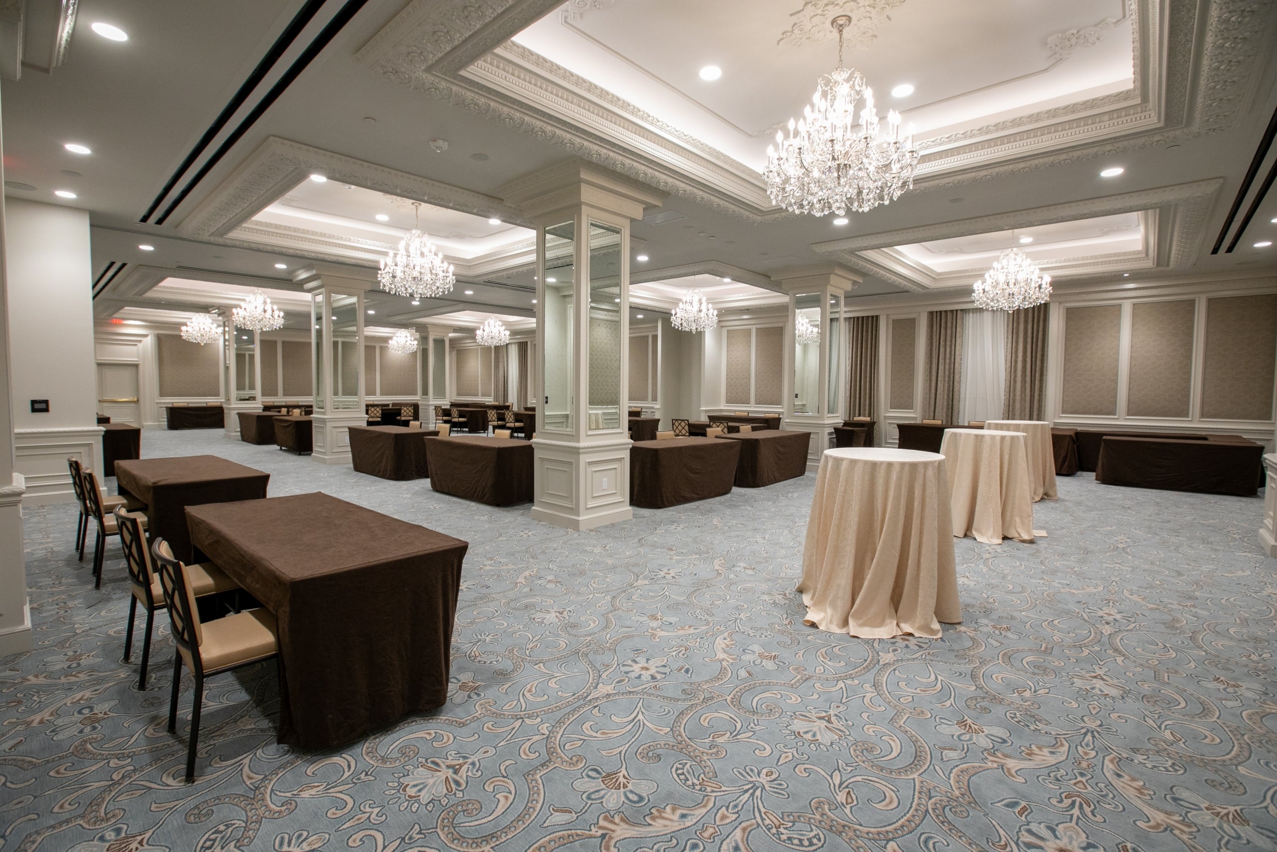 Grand New Orleans hotel ballroom with draped tables, sparkling chandeliers, and ornate blue carpet.