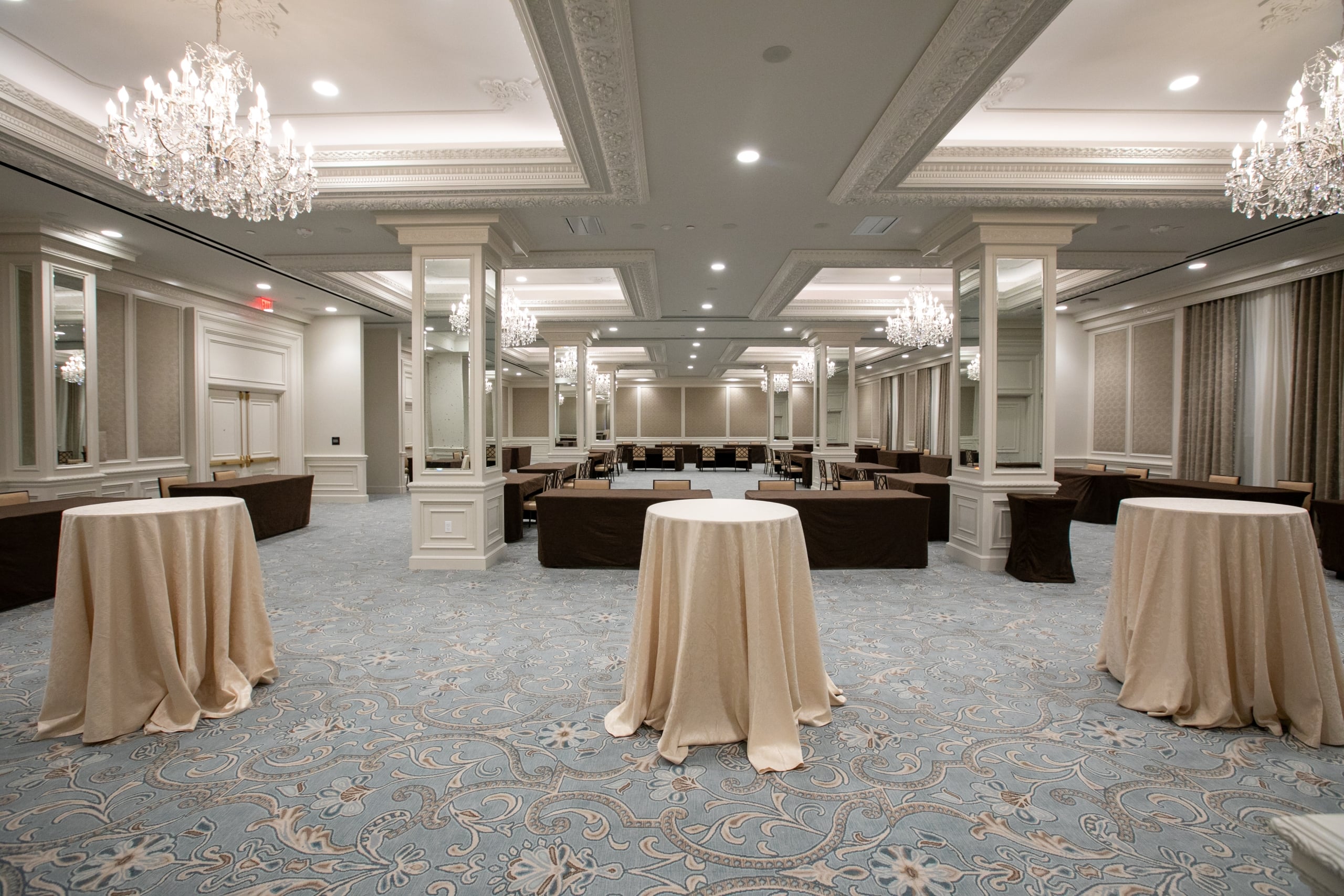 Elegant New Orleans hotel ballroom with round and rectangular tables, crystal chandeliers, and ornate carpet for events.