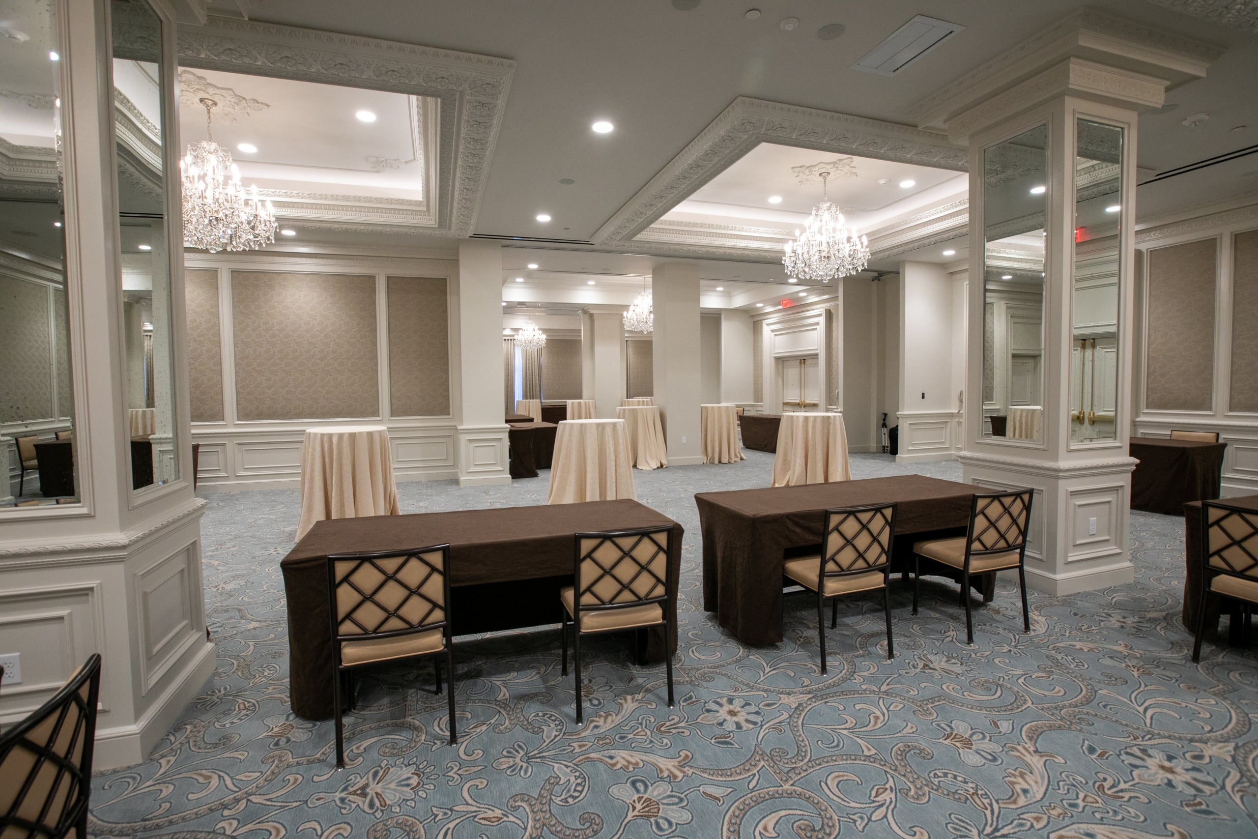 Lavish New Orleans hotel ballroom with ornate chandeliers, mirrored columns, and event tables.