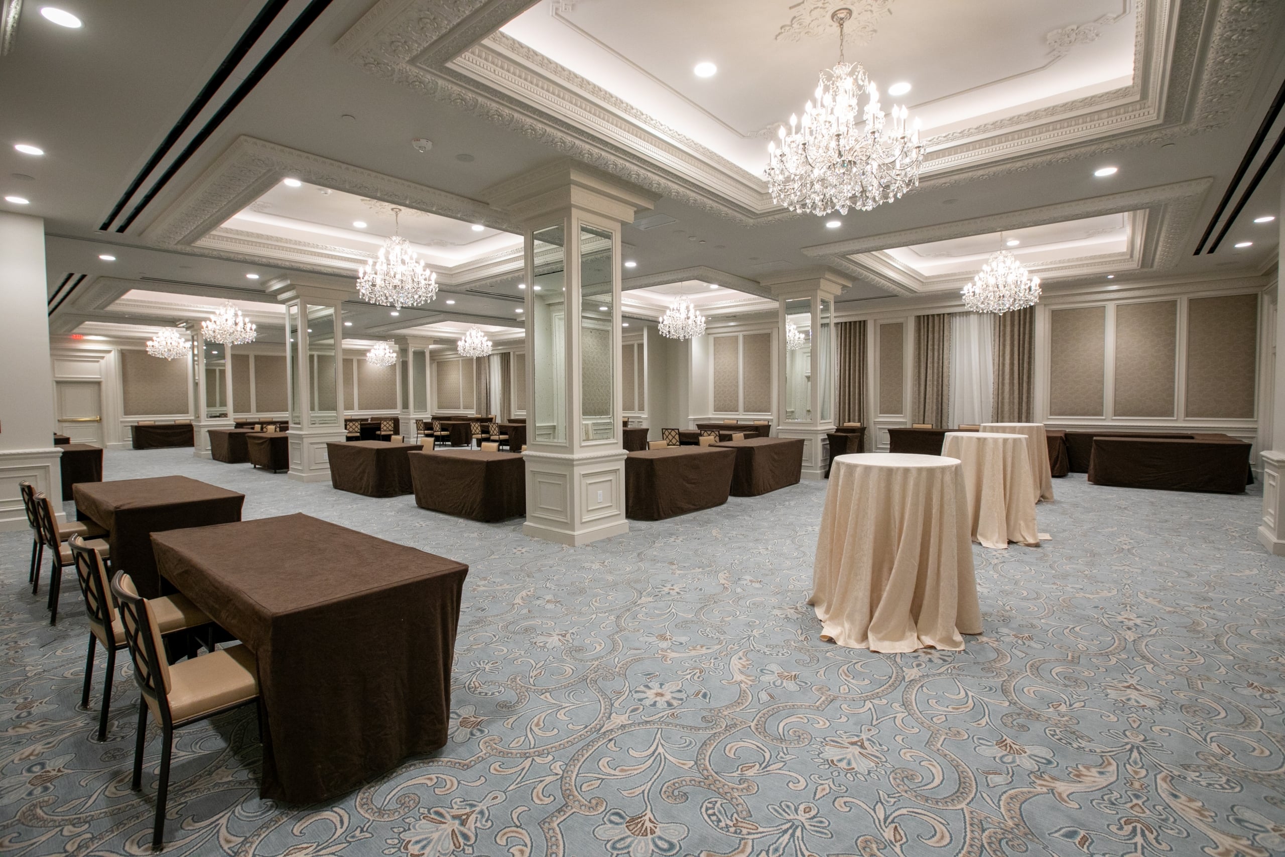 Elegant New Orleans ballroom featuring crystal chandeliers, mirrored pillars, and patterned blue carpet.