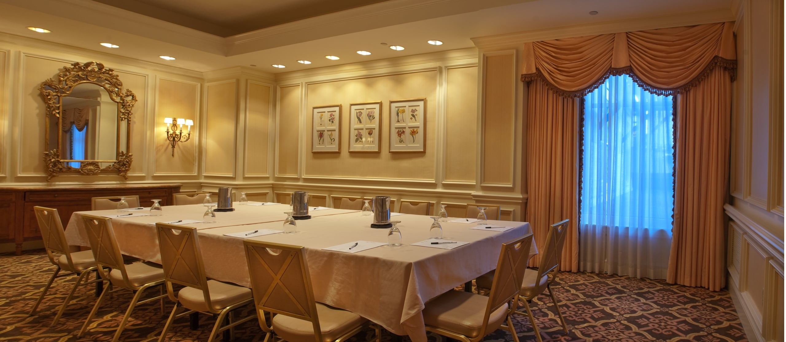 Elegant hotel meeting room in New Orleans with a long table, chairs, ornate mirror, and drapes.