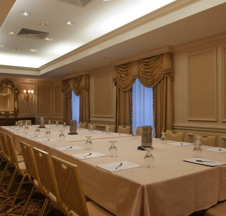 A long table with chairs in a meeting room with beige walls and curtains.