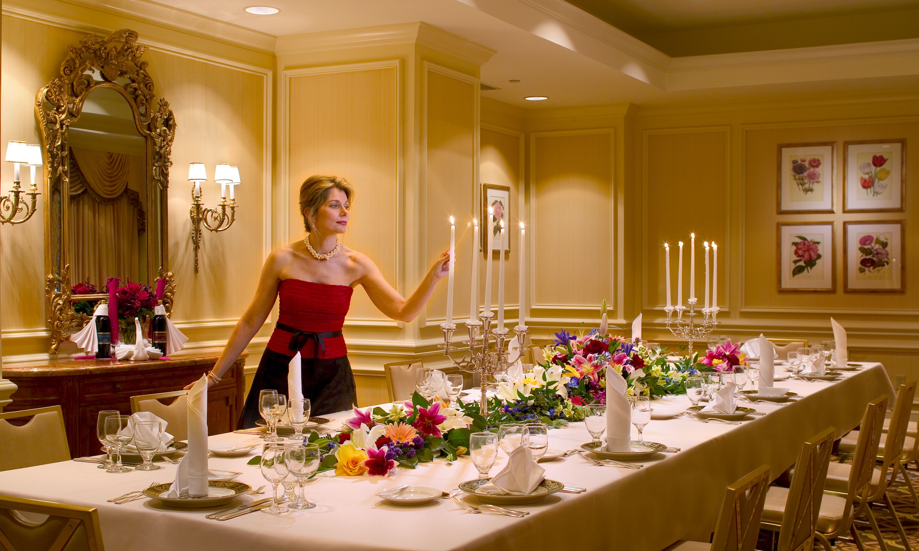 A woman in a red dress standing by a long dining table with flowers and candles