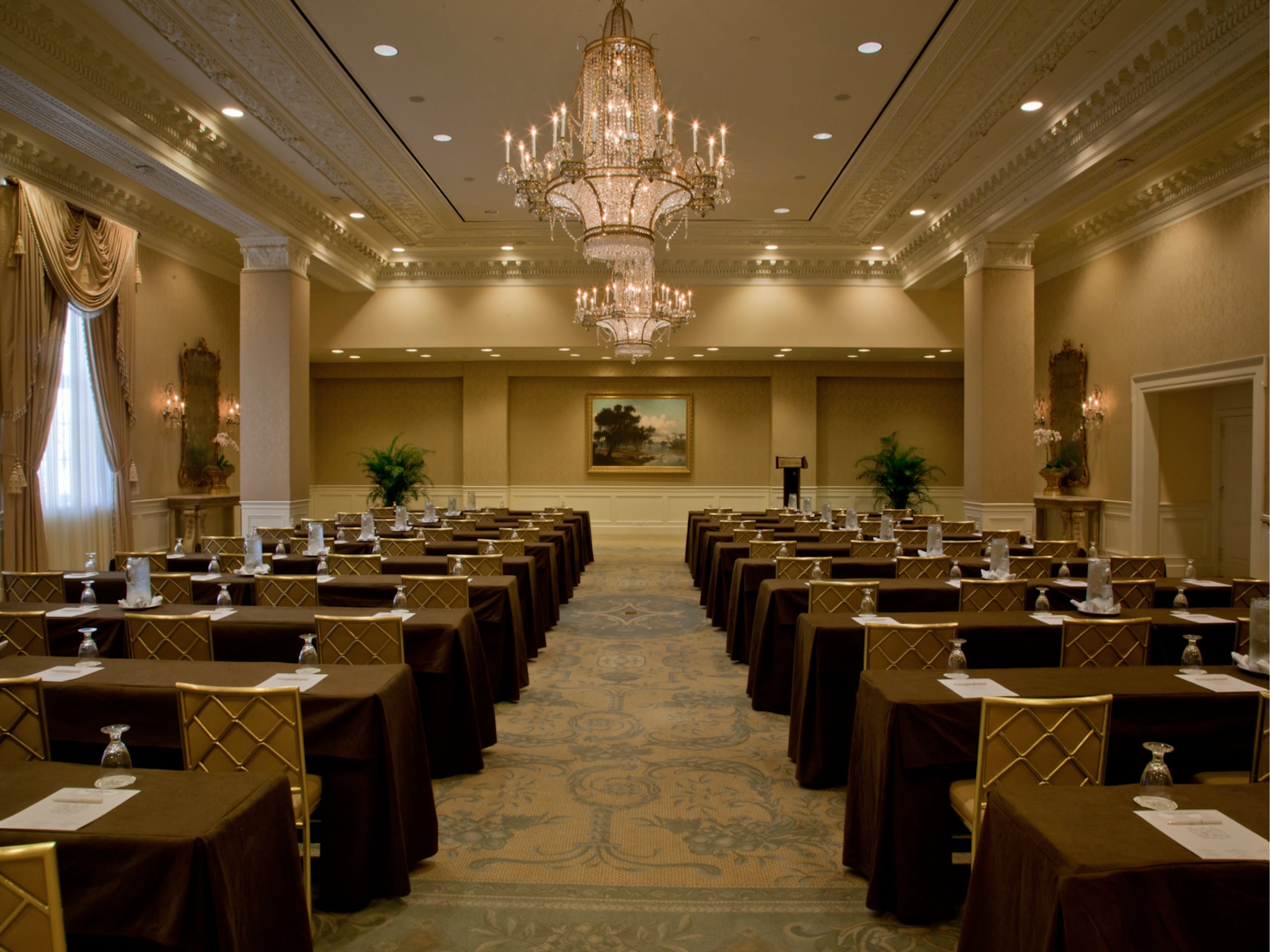 Luxurious New Orleans hotel ballroom set for a meeting, featuring elegant decor, chandeliers, and rows of tables with gold chairs.