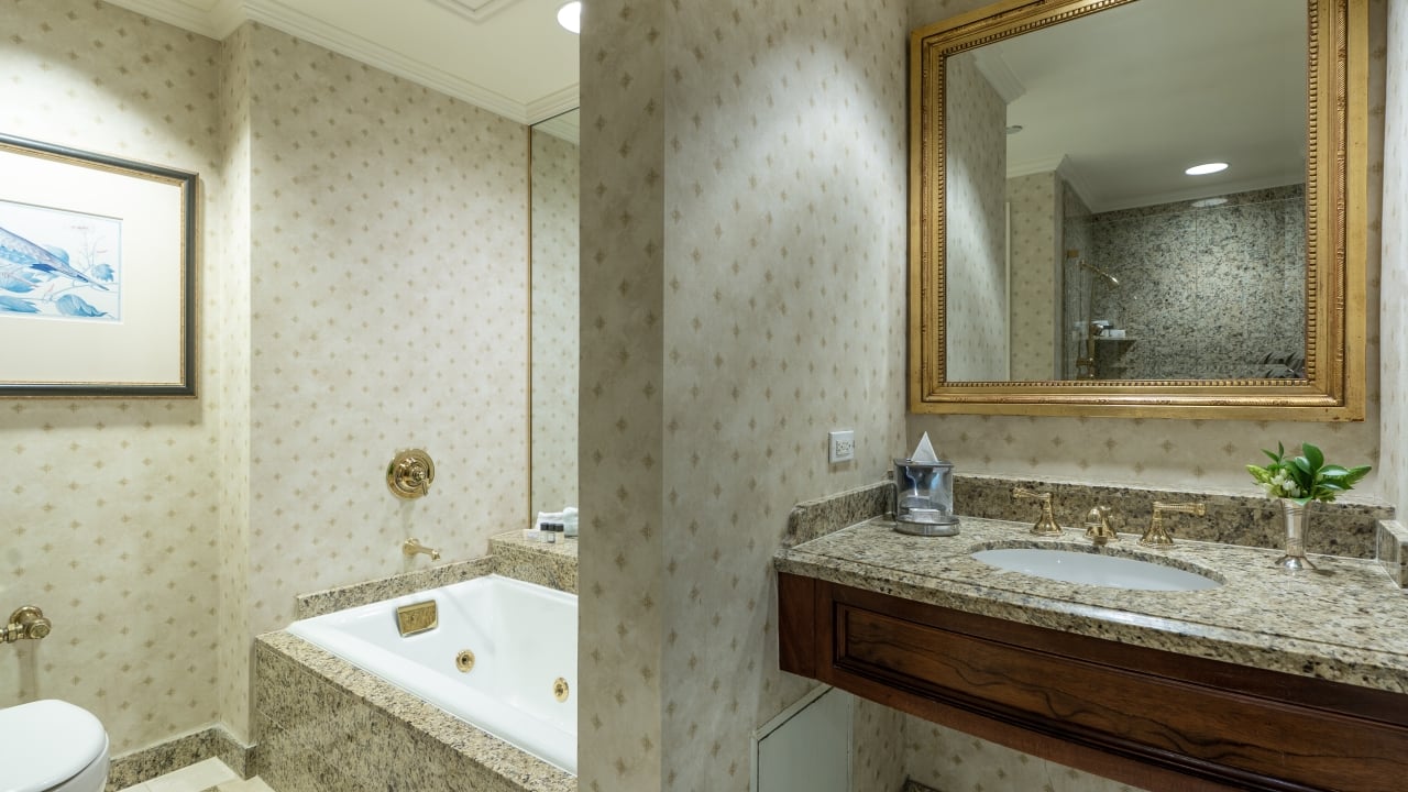 A bathroom with a built-in bathtub, toilet, and vanity with a granite countertop and gold fixtures.