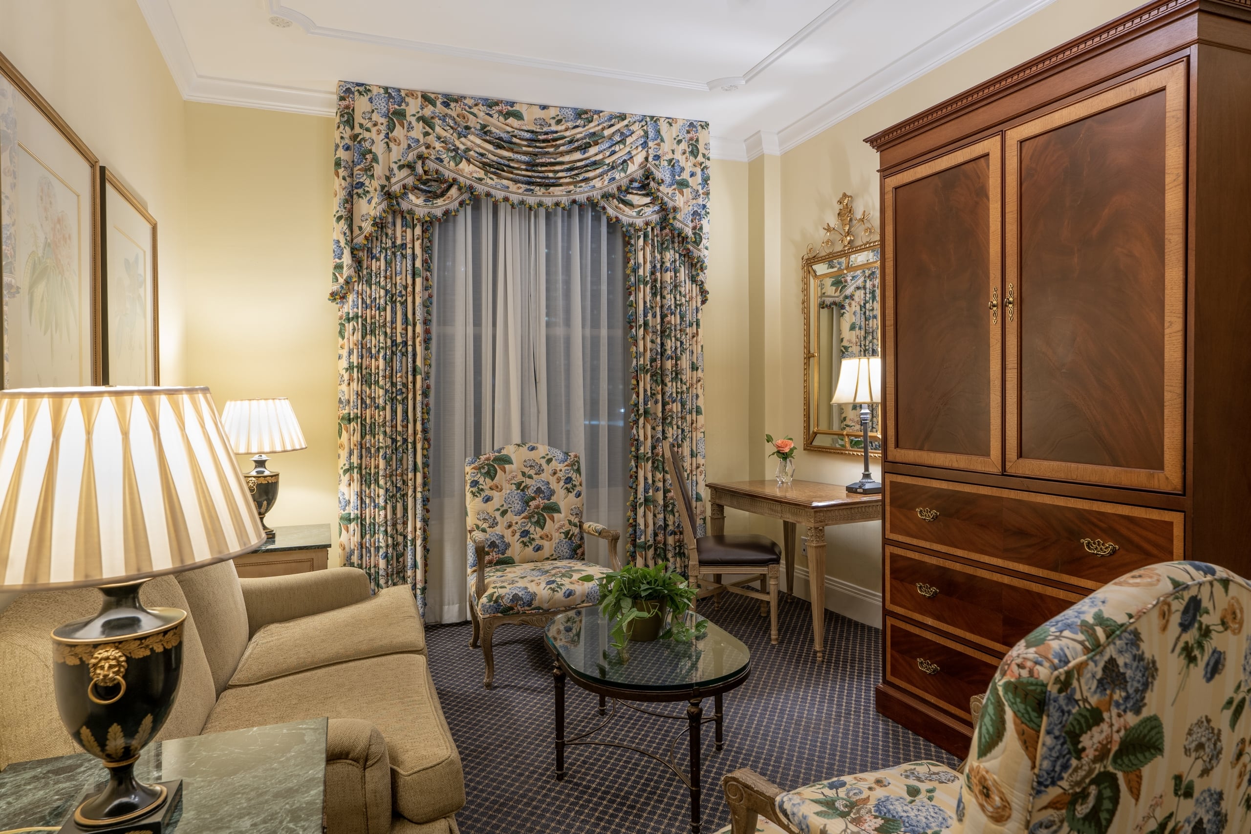 Elegant New Orleans hotel suite with floral chairs, a sofa, classic wood armoire, and an ornate gold mirror.