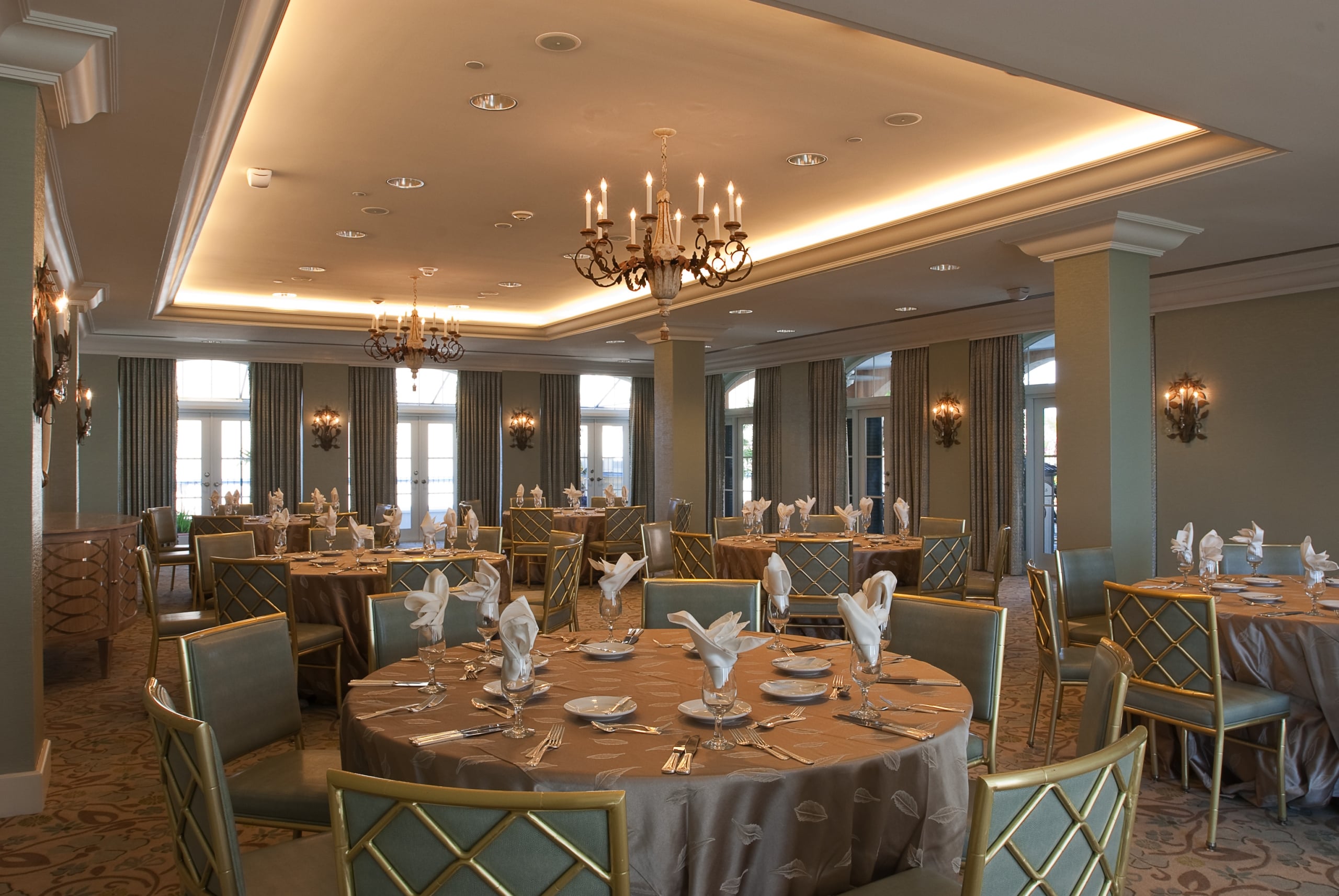 Elegant New Orleans event space with round tables, gold chairs, chandeliers, and French doors.