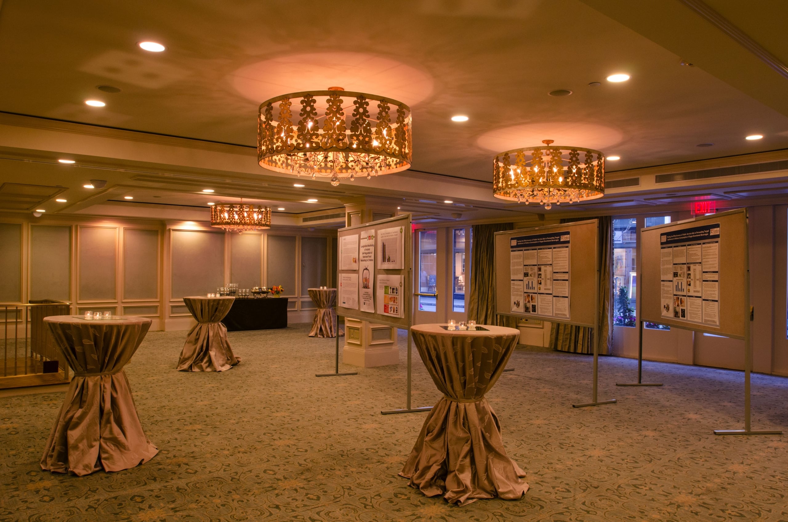 Elegant conference and event space in New Orleans with draped cocktail tables, chandeliers, and academic posters.