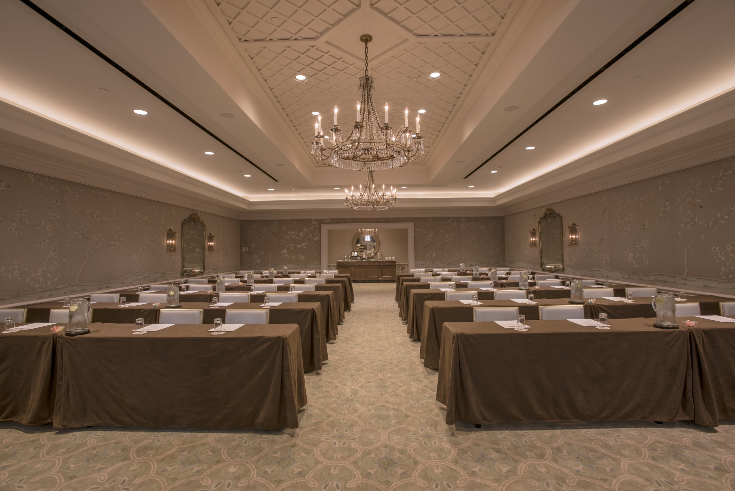 Elegant New Orleans meeting room setup with brown tables, a grand chandelier, and patterned walls.