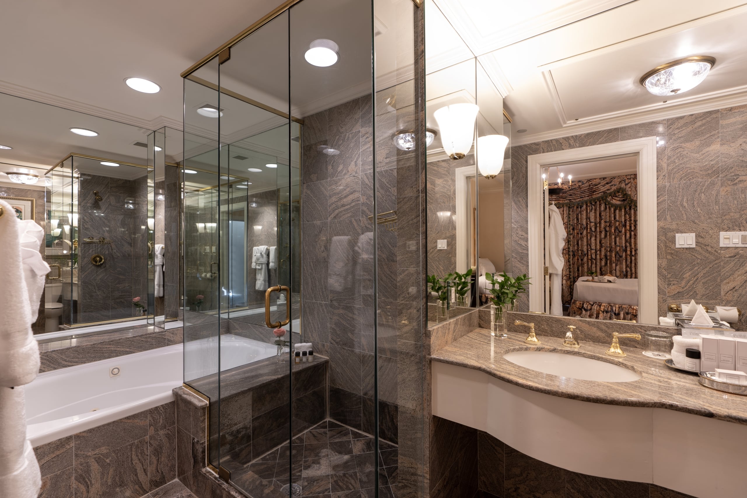 Elegant New Orleans short-stay bathroom with deep soaking tub, glass shower, marble vanity, and gold fixtures.