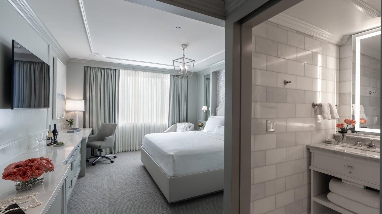 A wide view of a hotel room with a king bed, desk, TV, and bathroom.