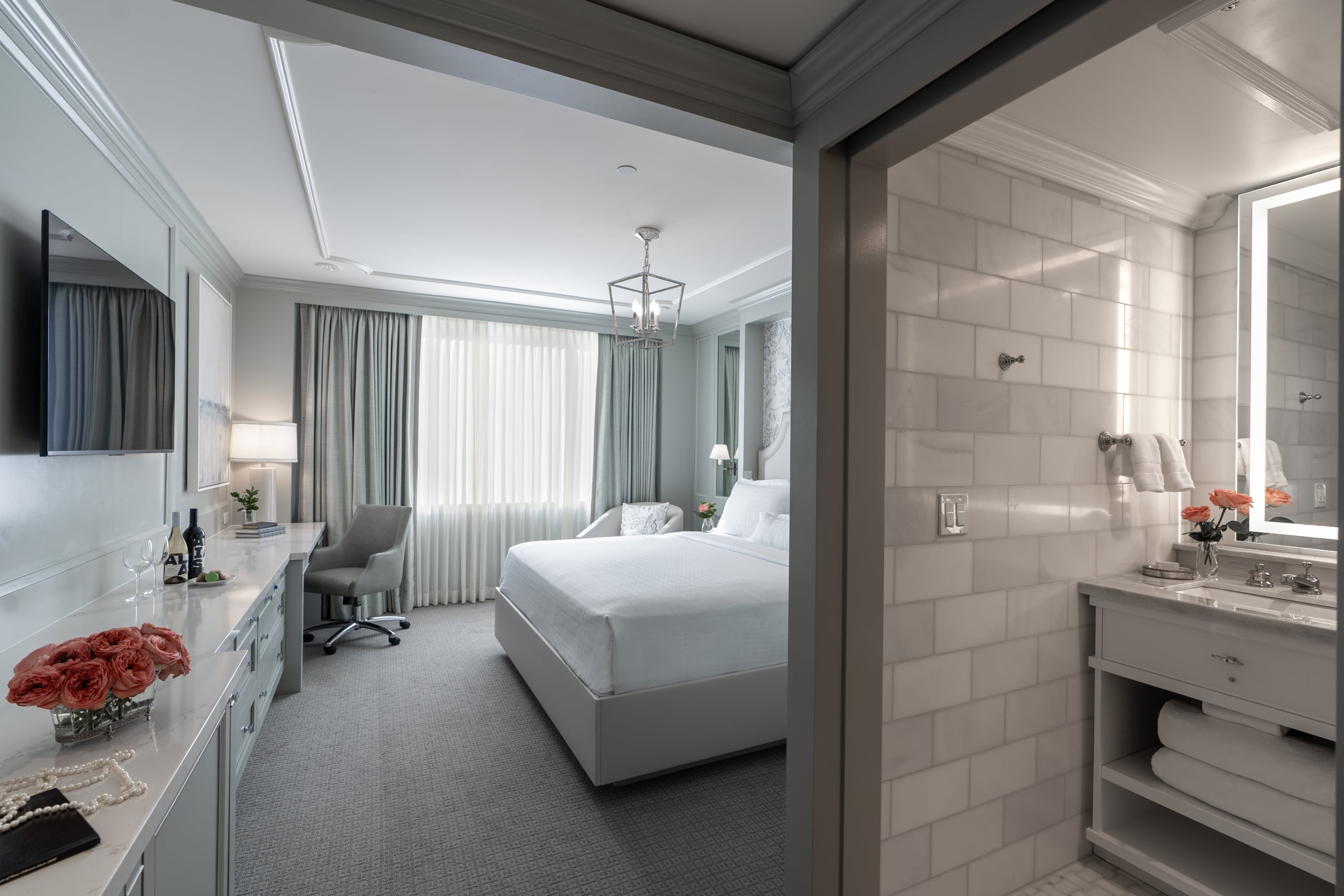 Luxurious hotel suite in New Orleans featuring a king bed, work desk, and an elegant bathroom with a lighted mirror.