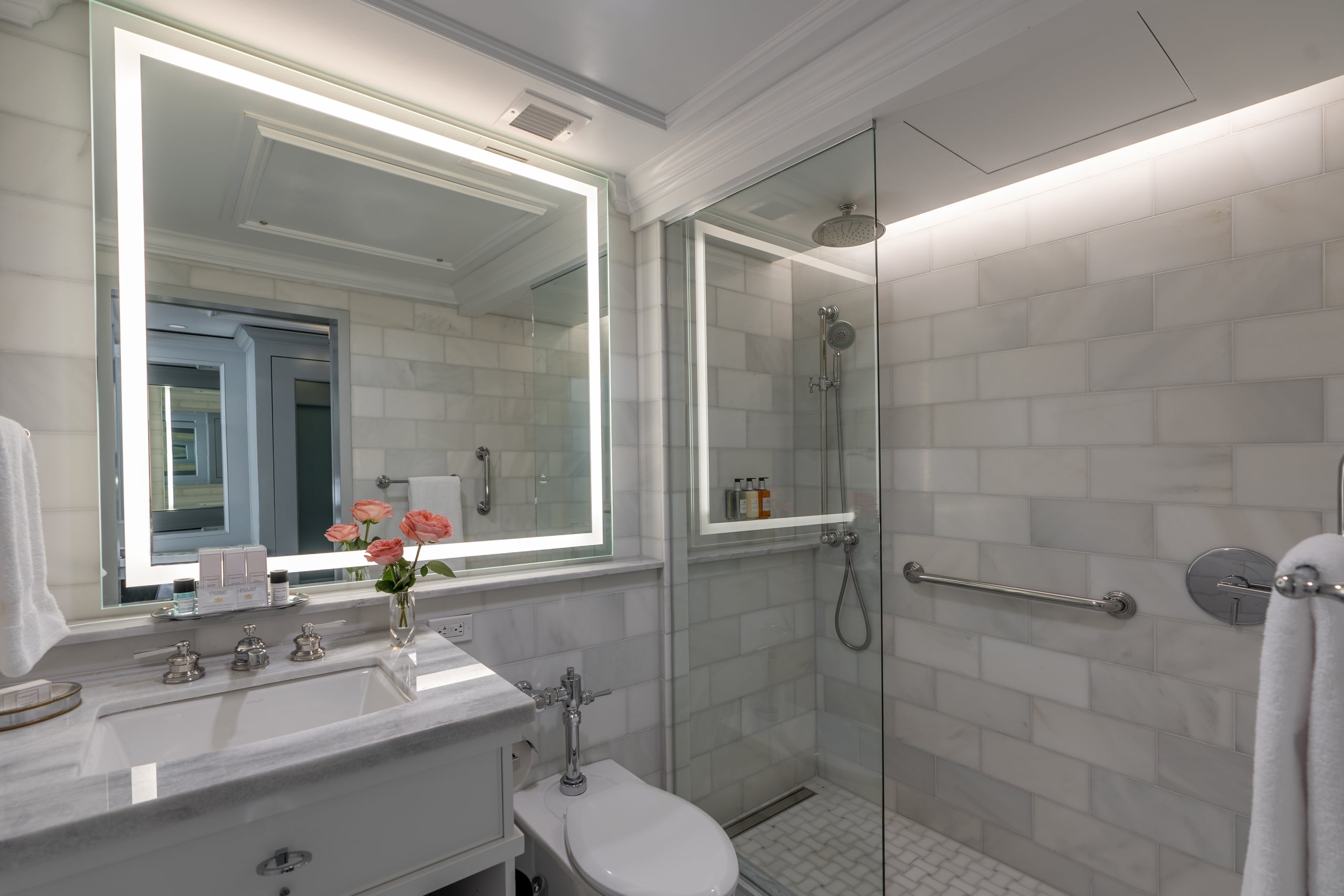Luxurious New Orleans hotel bathroom with marble vanity, lighted mirror, and accessible glass shower.