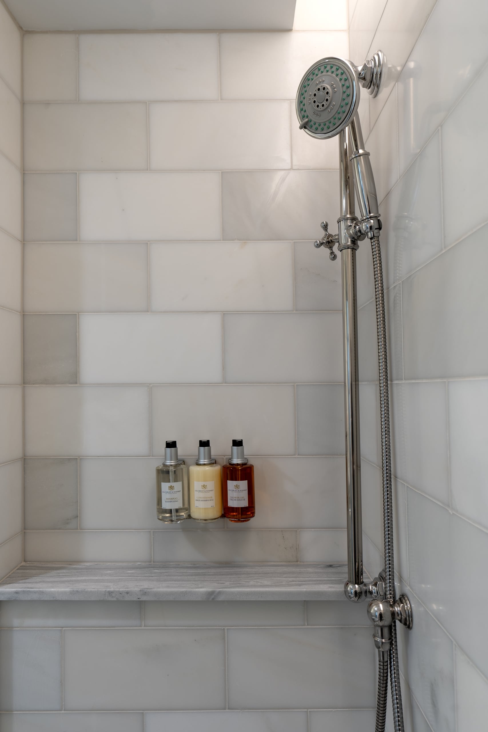 Luxury hotel shower in New Orleans with white subway tiles, marble shelf, and premium toiletries.
