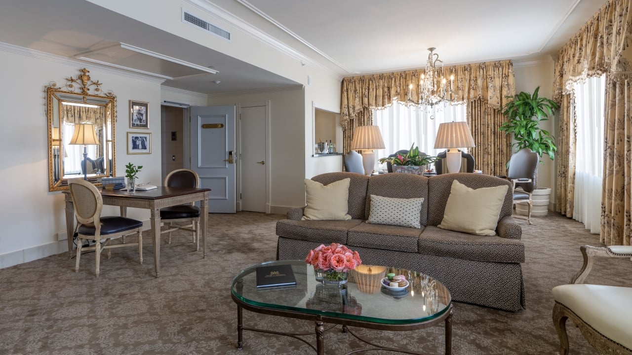 A wide view of a luxurious living room with a sofa, coffee table, desk, and chandelier.