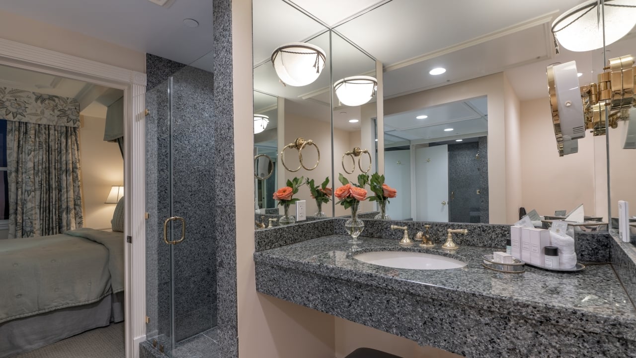 A bathroom vanity with a large mirror, granite countertop, and peach flowers.