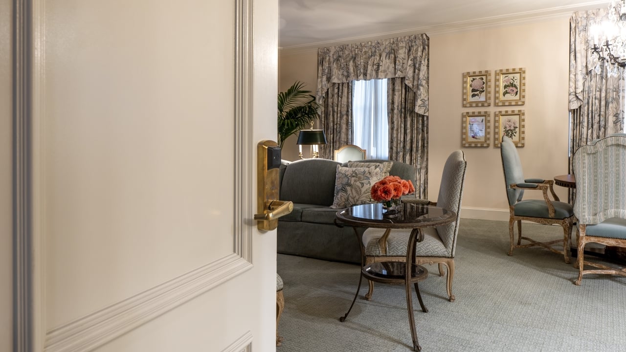 A wide view of a hotel room with a sofa, coffee table, armchairs, and a window.