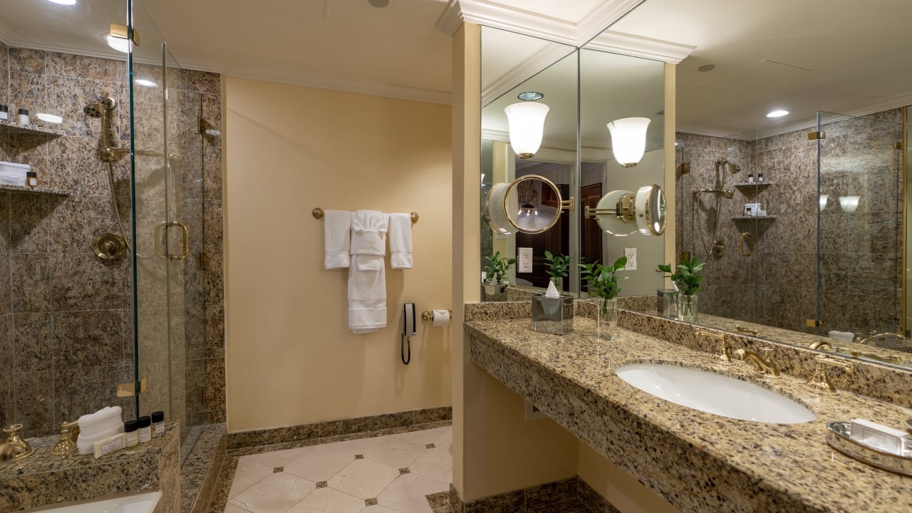 A luxurious bathroom with a double vanity, glass-enclosed shower, and marble tiles.