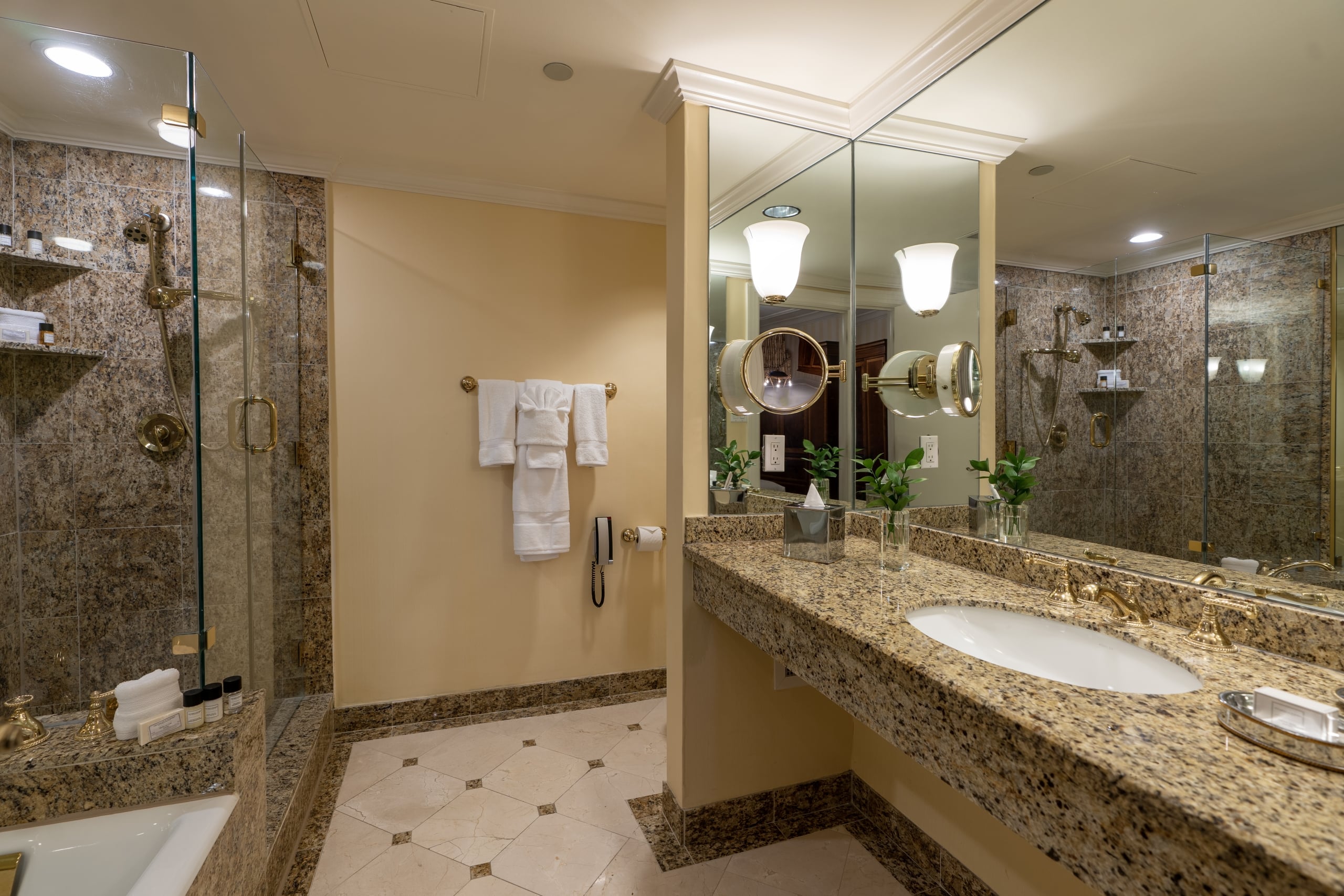 Luxury hotel bathroom in New Orleans with granite vanity, walk-in shower, and gold fixtures.