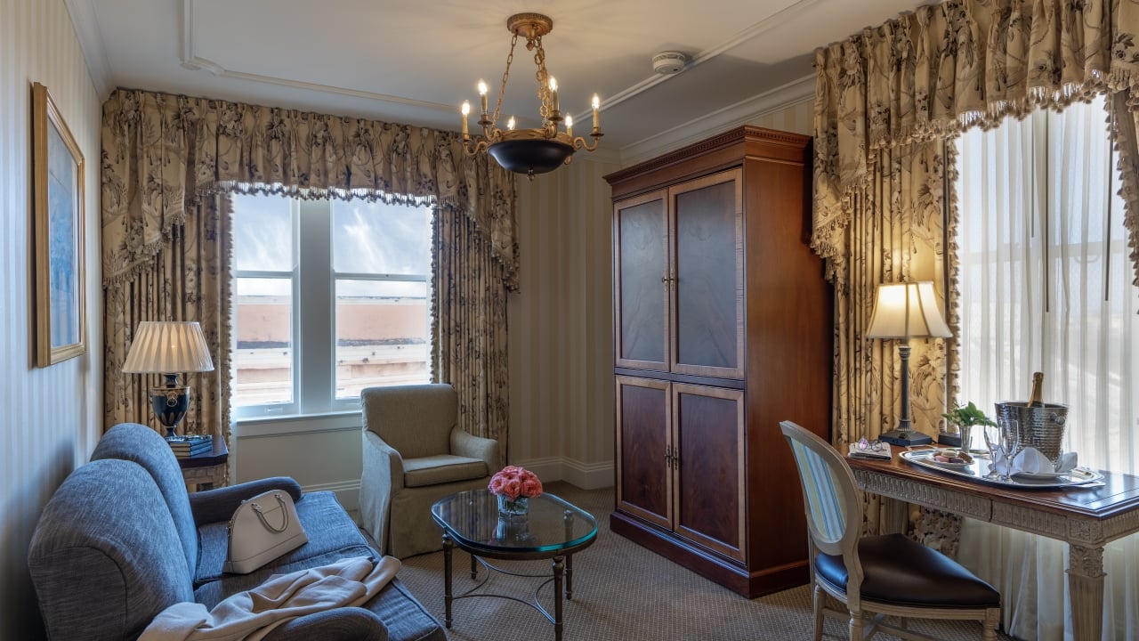 A wide view of a hotel room with a sofa, armchair, coffee table, desk, and chandelier.