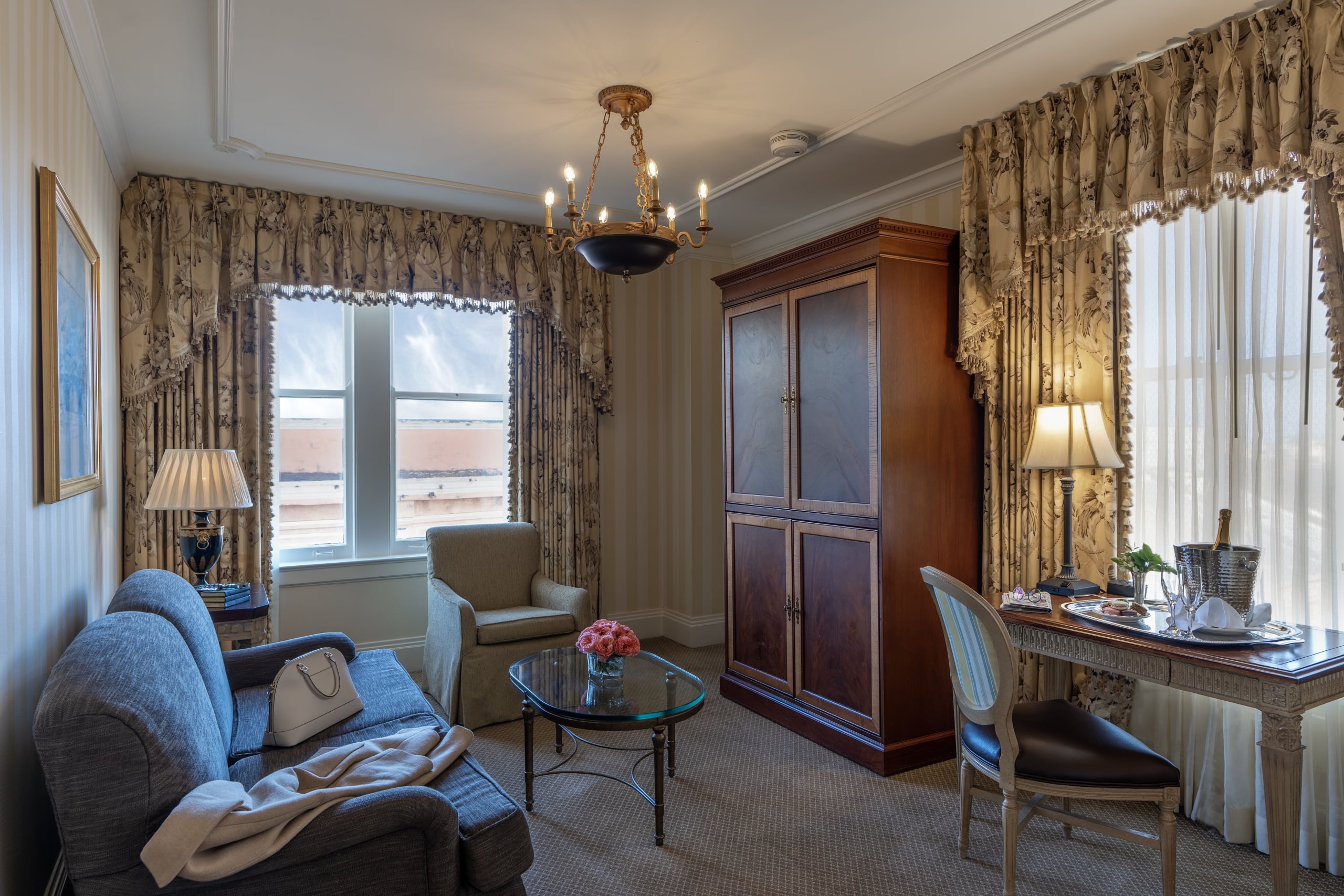 Elegant New Orleans hotel suite living room with sofa, ornate drapes, desk, and champagne.