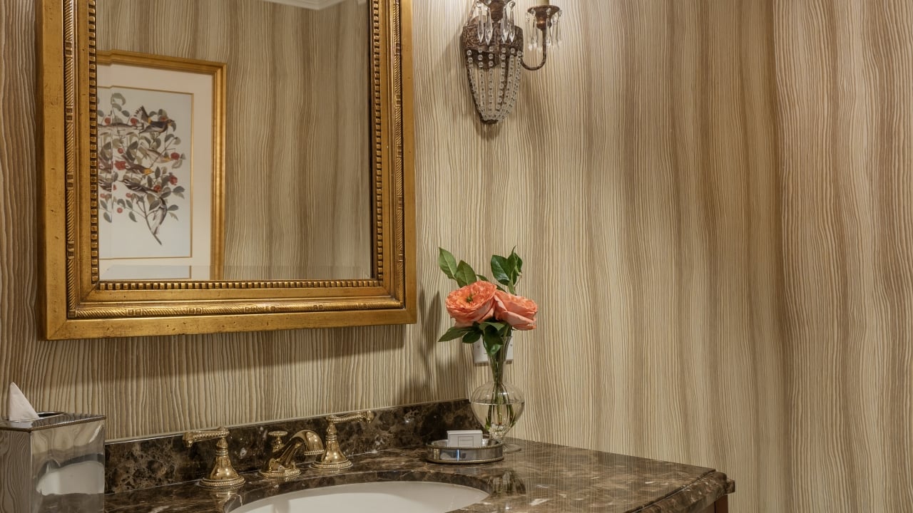A bathroom sink with a marble countertop, gold faucet, and a mirror with a gold frame, with pink roses in a vase.