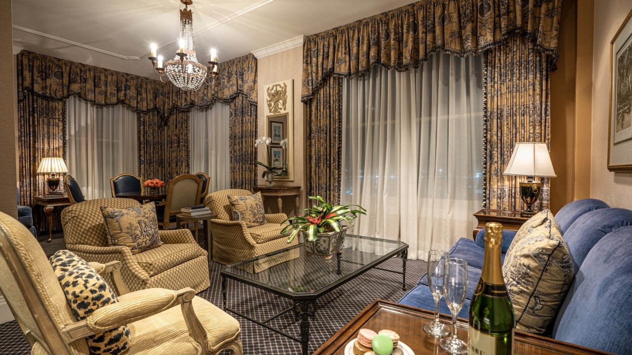 A luxurious living room with a blue sofa, armchairs, a glass coffee table, and a chandelier.