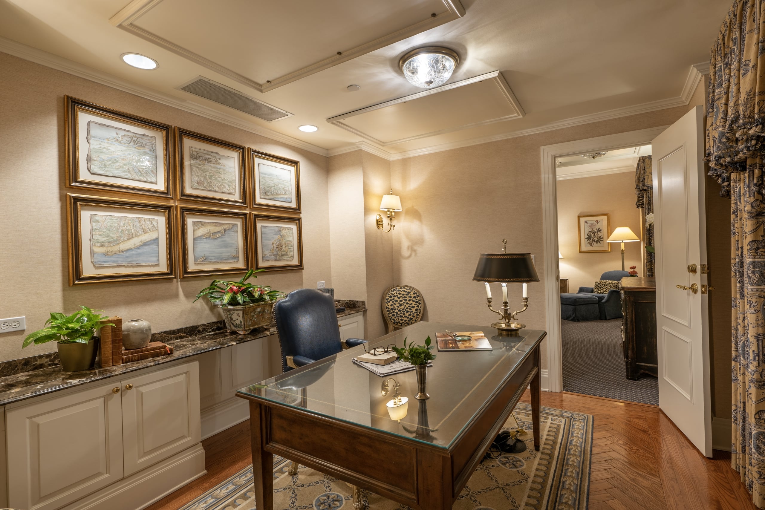 Luxurious New Orleans suite office with historic maps, a glass desk, and blue leather chair.